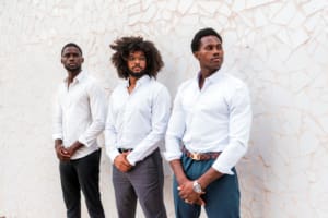 Three Confident Multiracial Businessmen Standing Against A Textured White Wall Outdoors