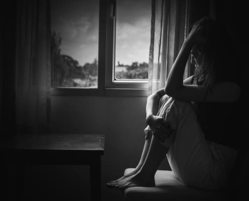 Depress Woman Sitting On Chair In Room Near Window In White Tone, Sadness And Depress Concept