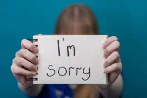 A Woman Holds A Card With The Words Sorry In Her Hands