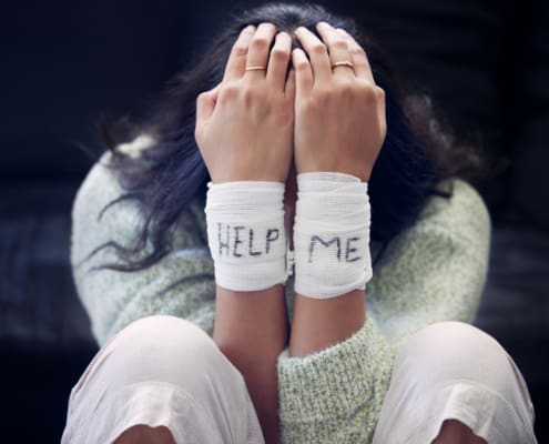 Shot Of A Young Woman With Bandages Wrapped Around Her Wrists Showing “help” Written On Them